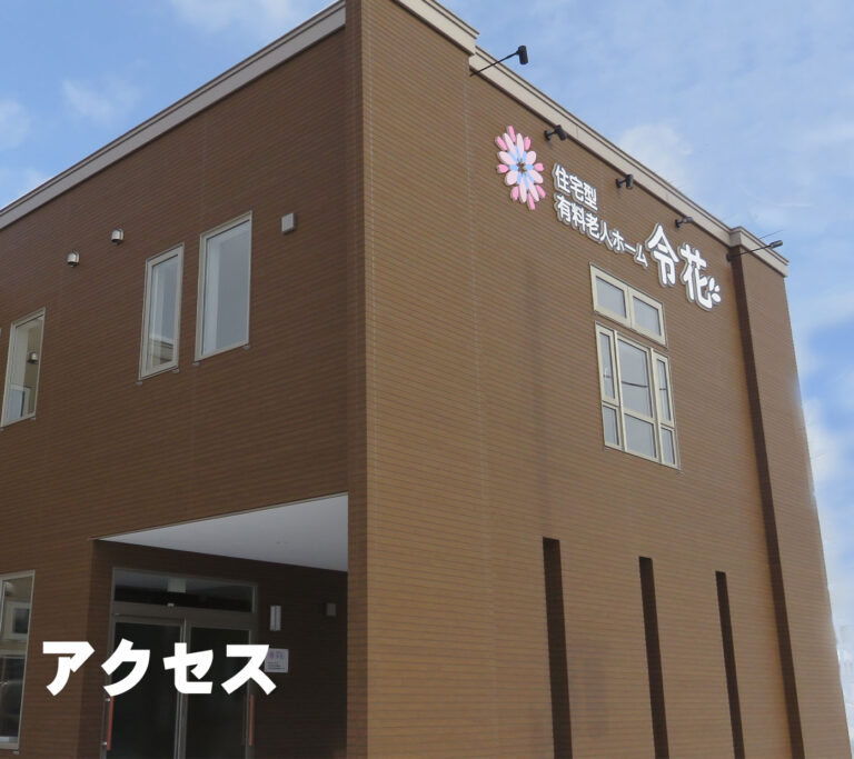 茶色のサイディング外壁を持つ介護施設の建物外観。ピンク花のロゴと施設名が見える。